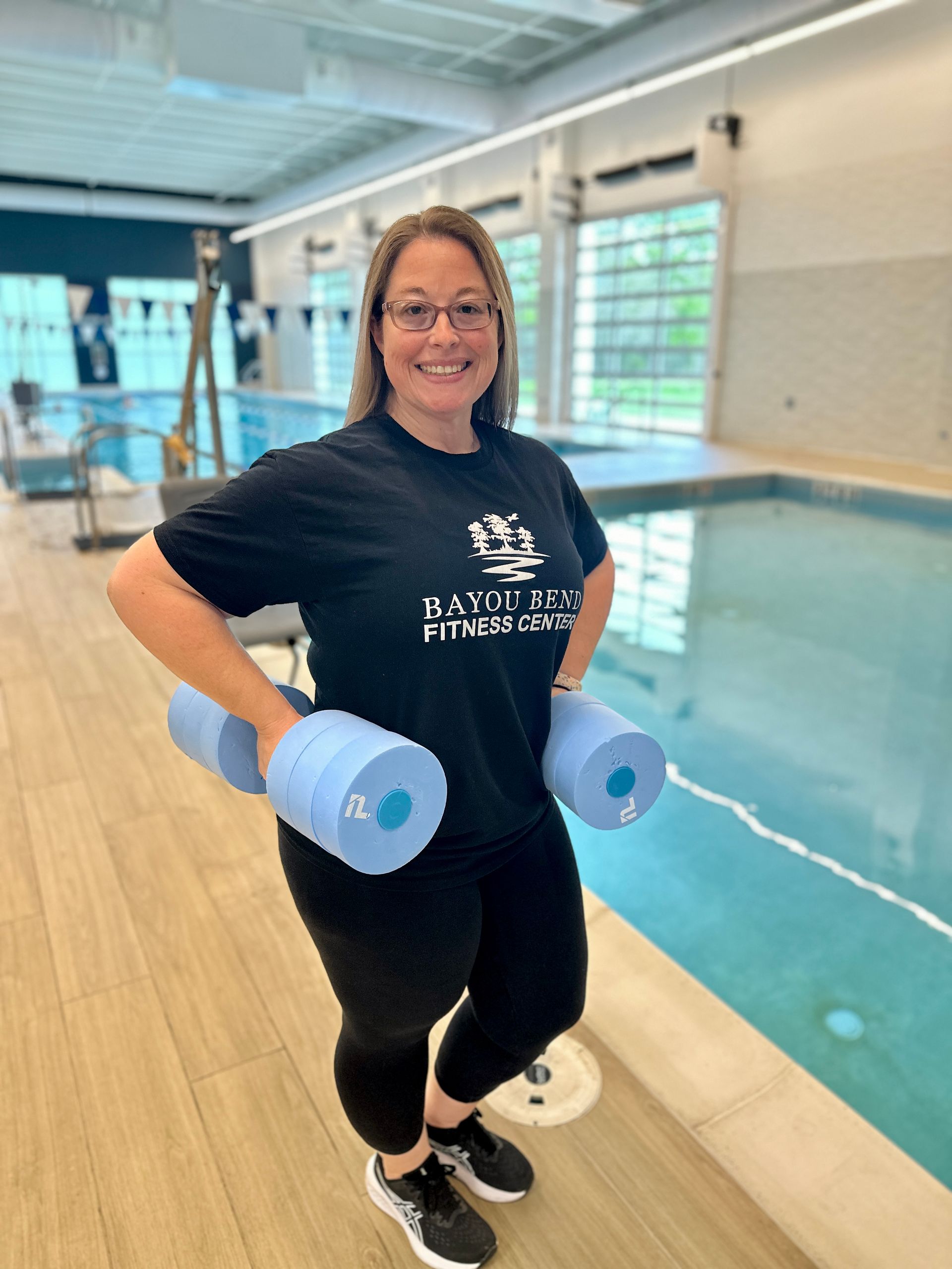 A woman is standing in front of a swimming pool holding dumbbells.