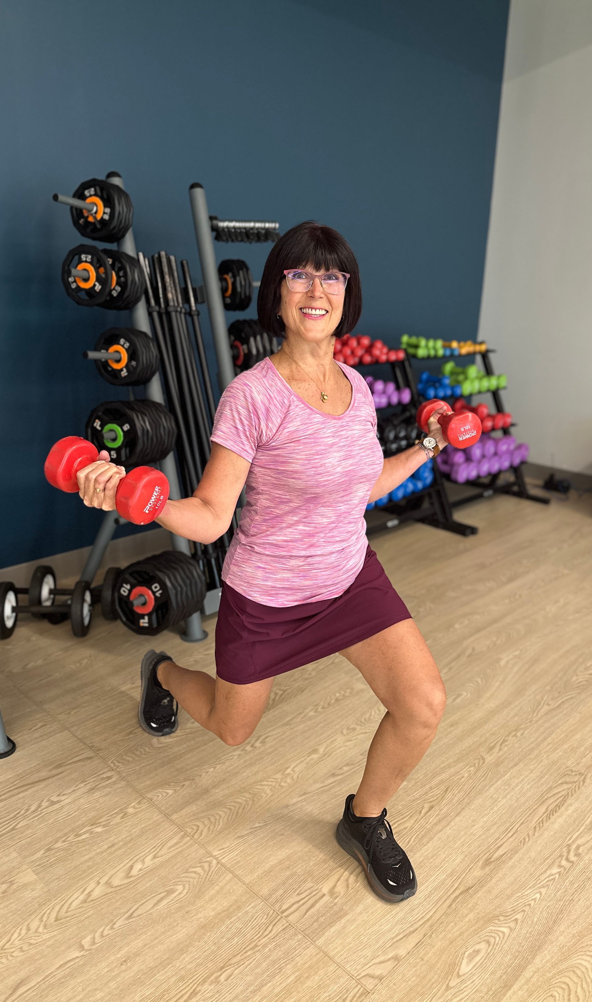 A woman is holding two red dumbbells in a gym.