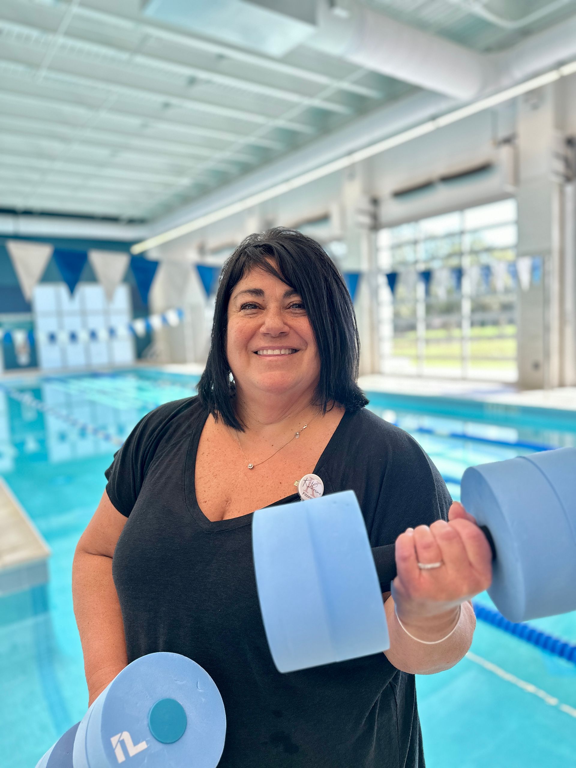 A woman is holding a pair of dumbbells in front of a swimming pool.