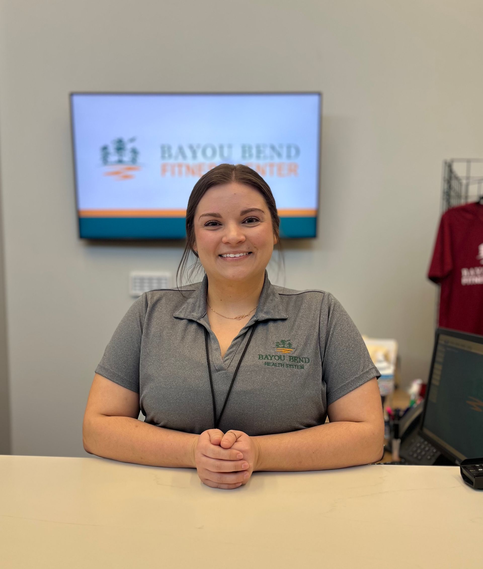 A woman in a grey shirt is sitting at a desk in front of a tv.