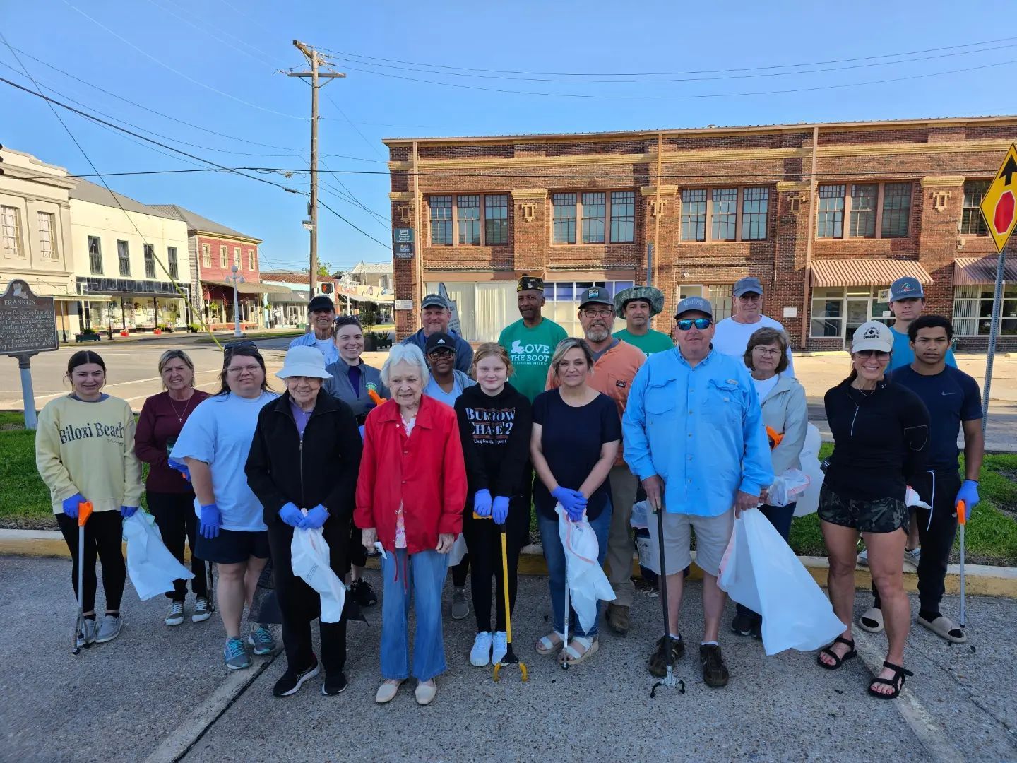 A group of people are standing in front of a building holding trash bags.
