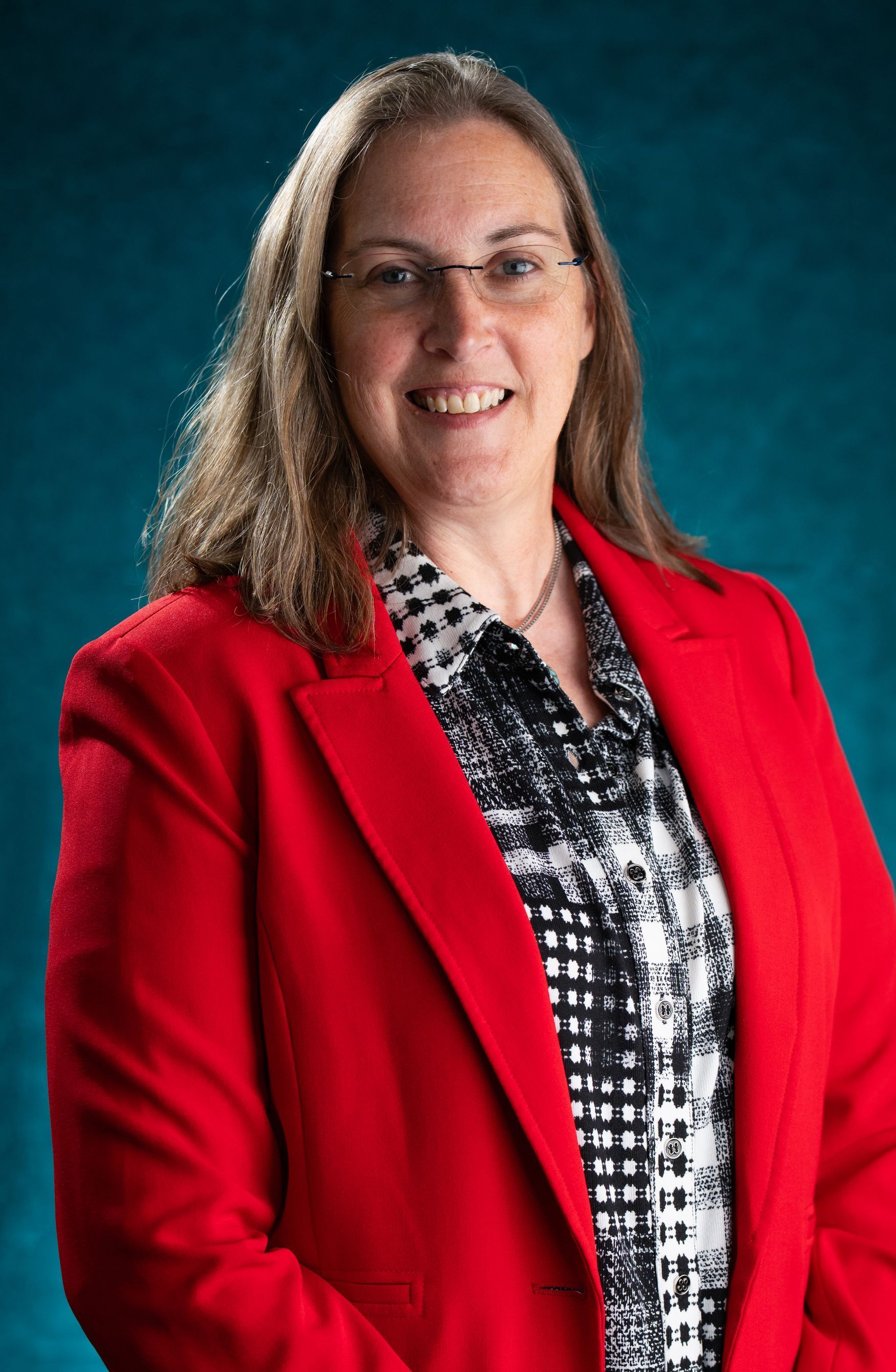 A woman wearing a red jacket and glasses is standing in front of a blue background.