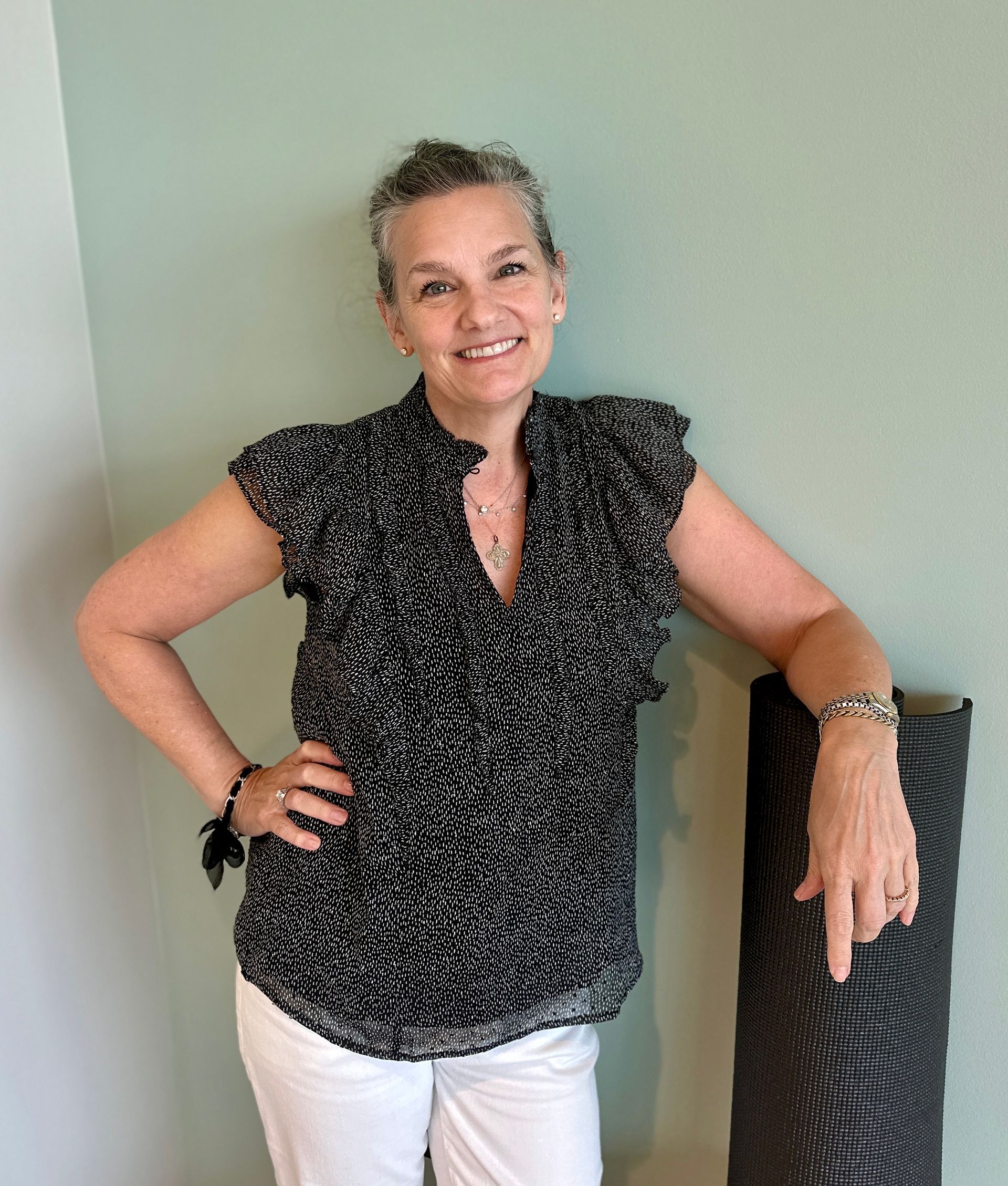 A woman in a black and white top and white pants is standing next to a vase.