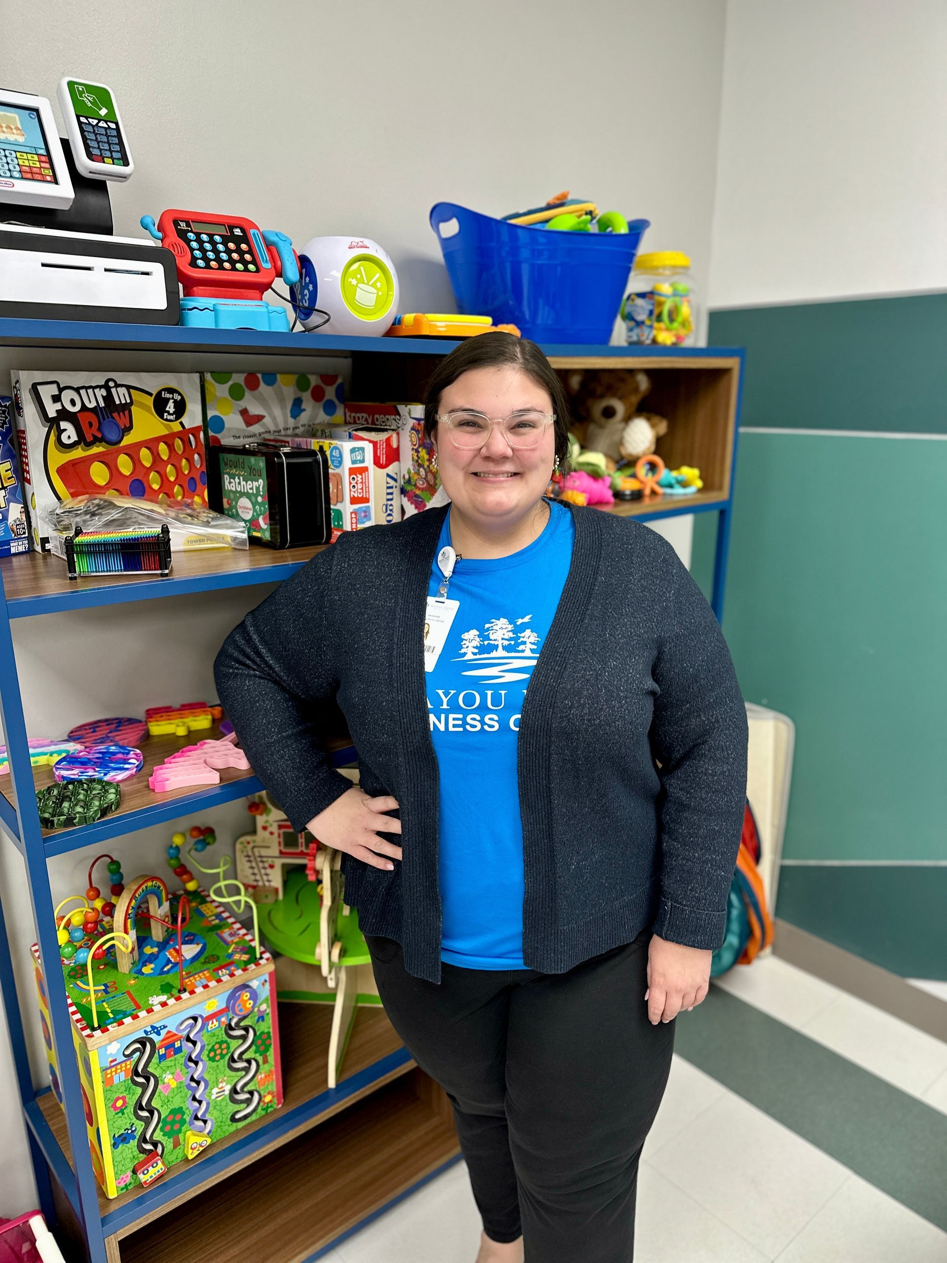A woman in a blue shirt is standing in front of a shelf full of toys.