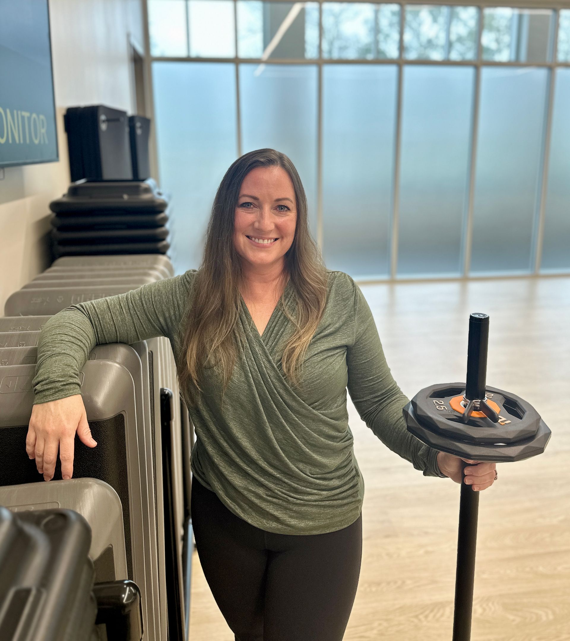 A woman in a green shirt is holding a barbell in a gym