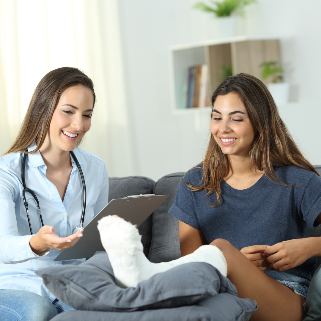 A woman with a cast on her leg is sitting on a couch talking to a doctor.