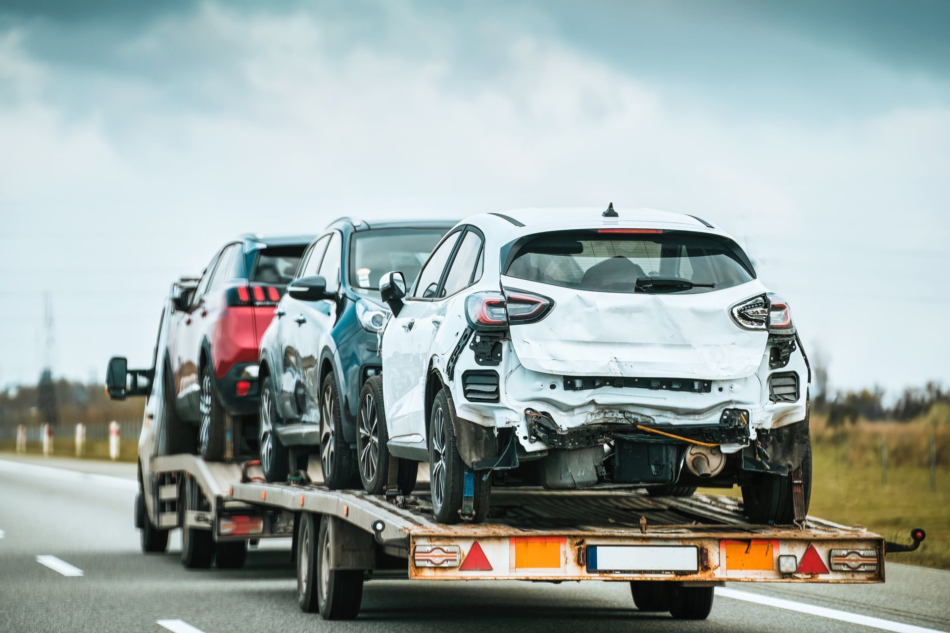 Cars loaded on a car carrier, including a white damaged vehicle, traveling on a highway.