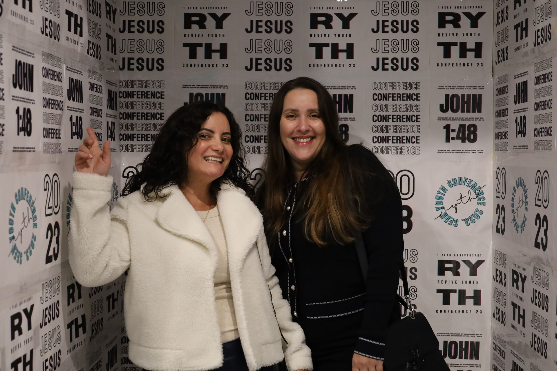 two women are posing for a picture in front of a wall that says jesus