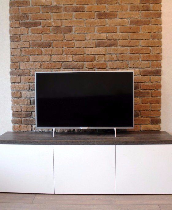 flat-screen TV on media stand in front of brick wall
