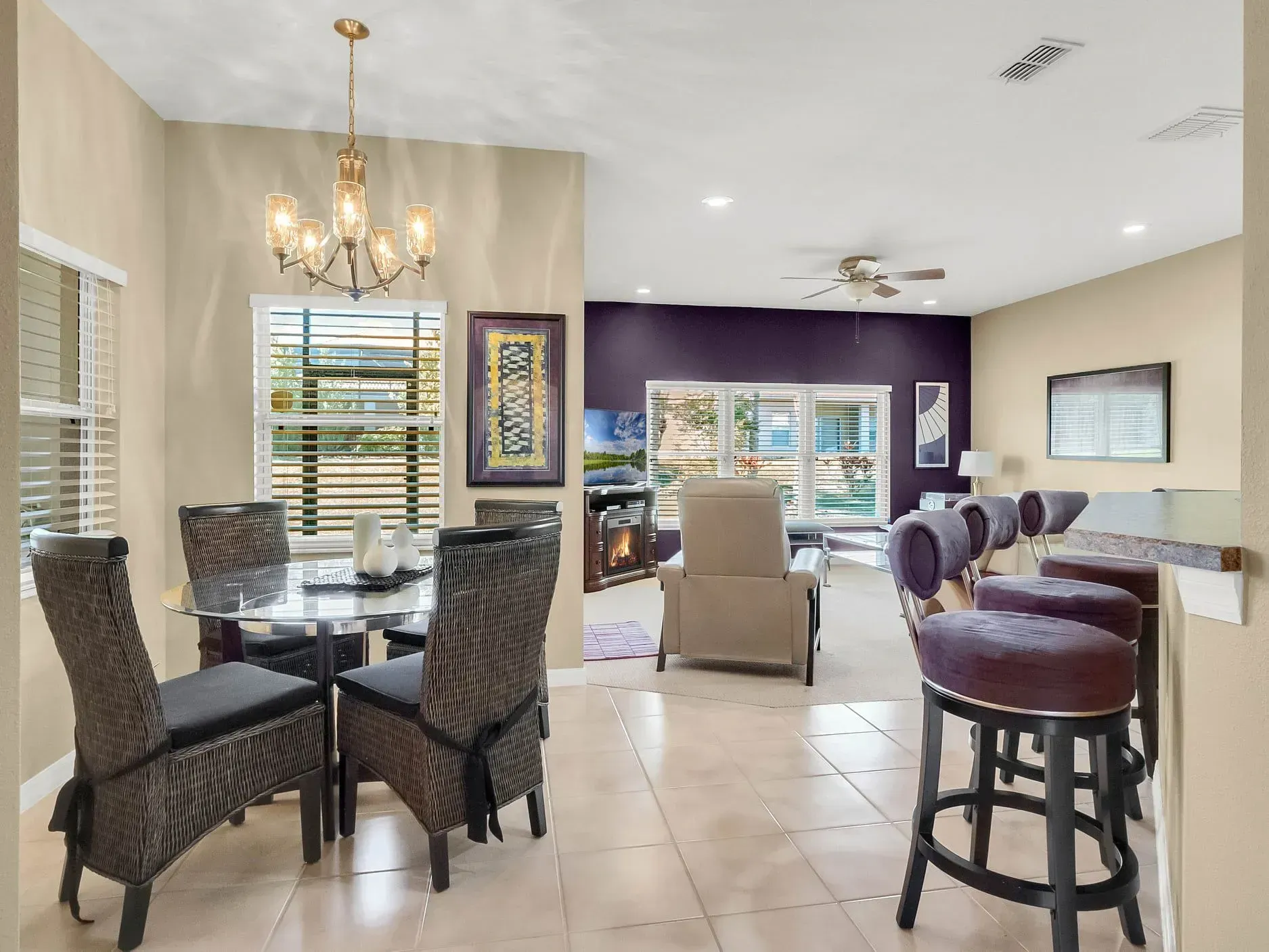 A dining area with a glass table and four woven chairs, leading to a living room with an armchair and bar seating.