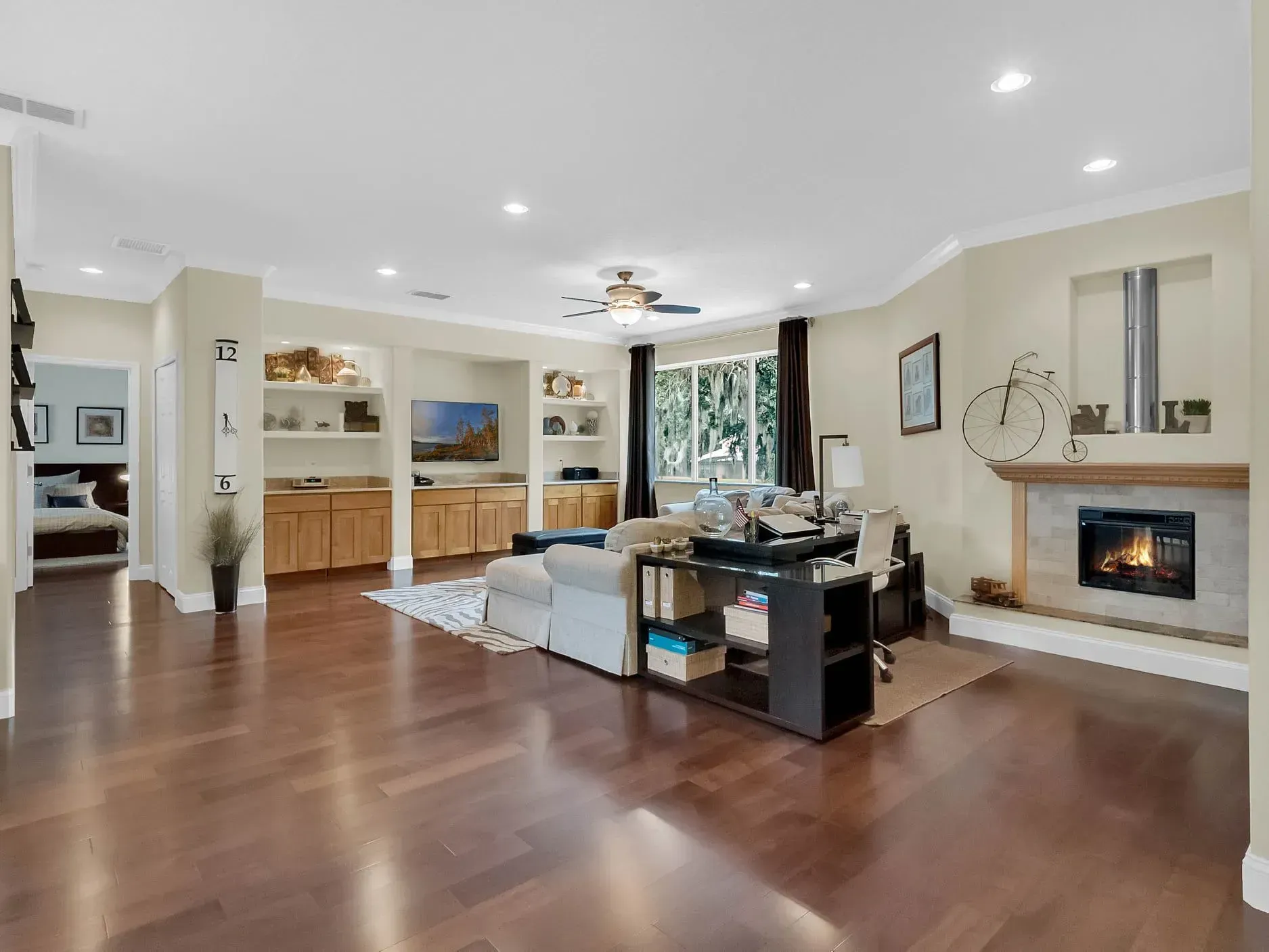 A spacious living room featuring hardwood floors, built-in wooden shelving, a fireplace, and a couch.