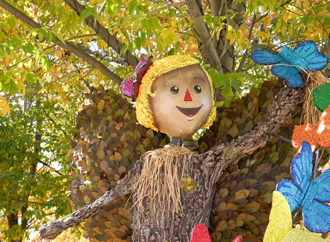 Fairy sculpture made of wood, with a smiling face, arms outstretched, surrounded by colorful butterflies.