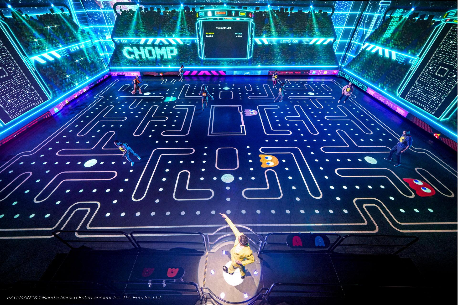 Giant Pac-Man game arena; players as Pac-Man and ghosts navigate the maze. Bright neon blue and white lighting.