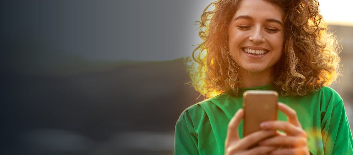 A woman is smiling while looking at her cell phone.