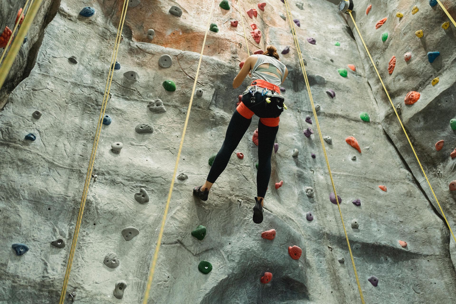 Woman in harness climbs a colorful indoor rock wall.
