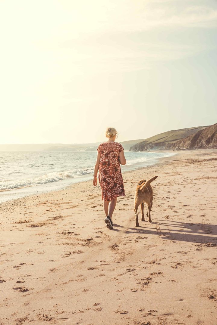A woman is walking her dog on the beach.