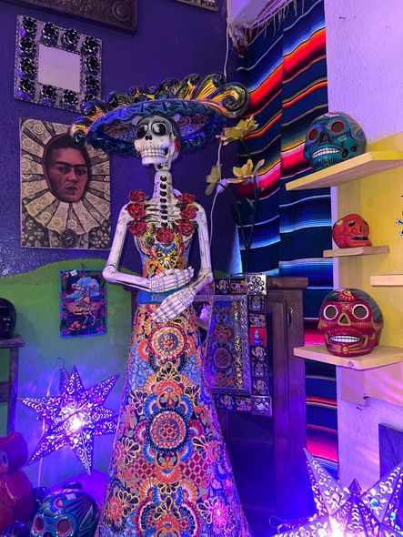 A skeleton in a colorful dress is standing in a room surrounded by skulls.