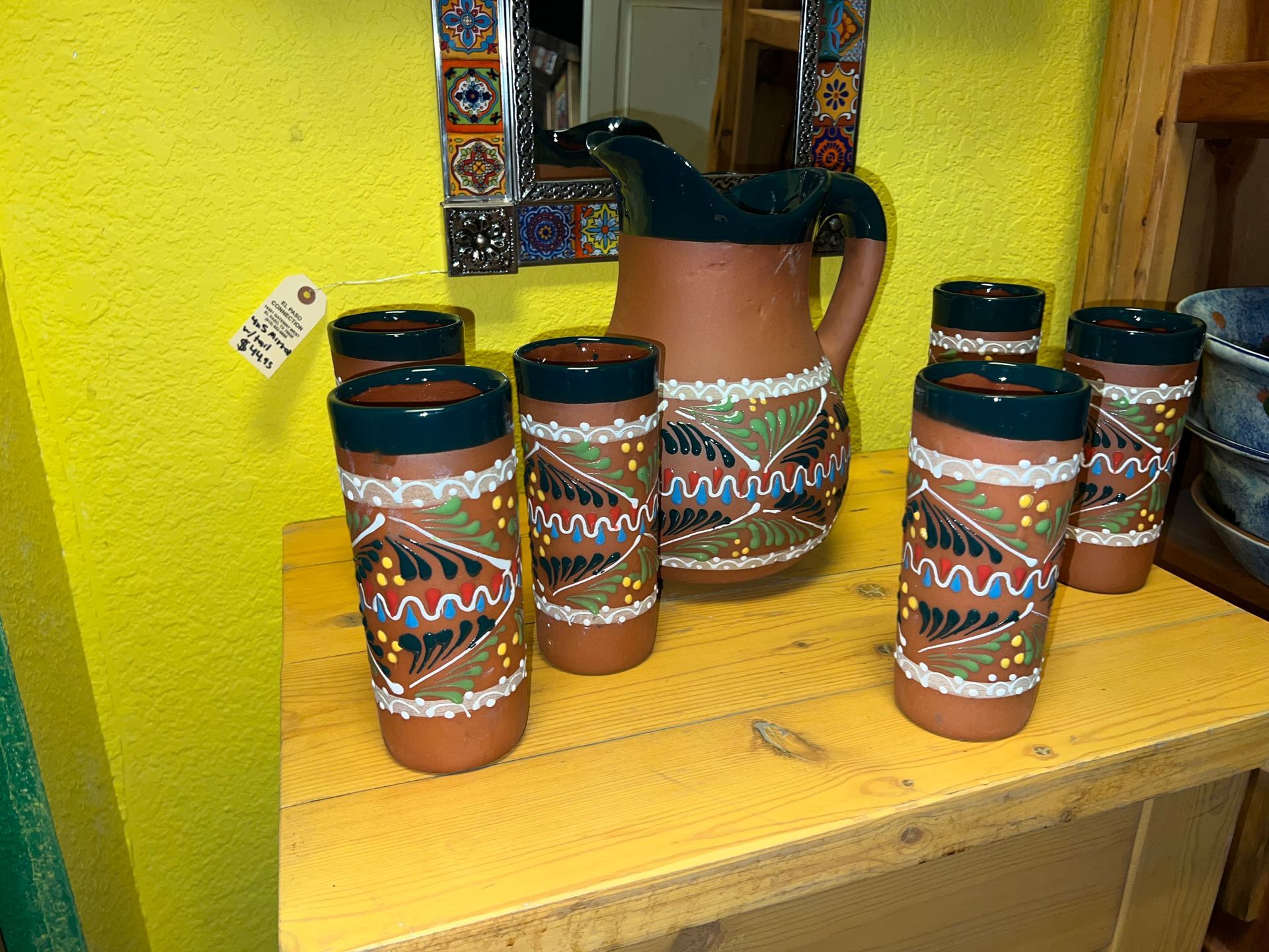 A pitcher and six glasses are sitting on a wooden table.