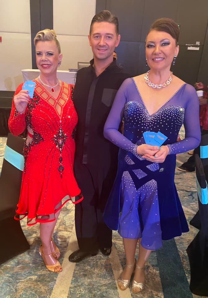 Three people in formal attire: woman in red dress, man, woman in blue dress, holding award cards.