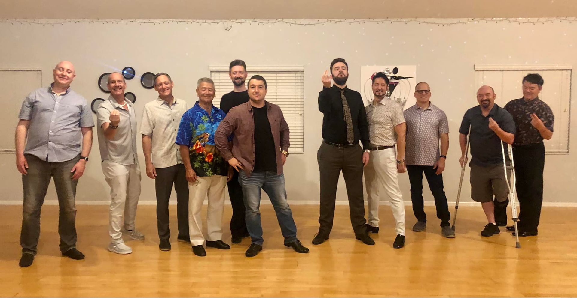 A group of men posing in a dance studio. Some have their hands up, others are leaning, and one is using a cane.
