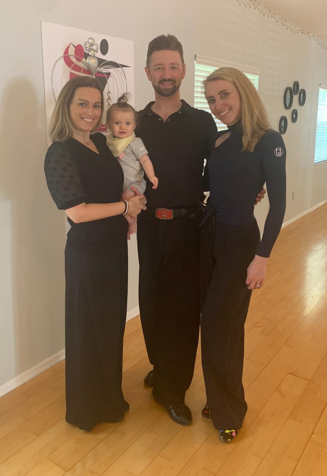 Family of four poses for a photo: woman with baby, man, and another woman, all wearing black clothing.