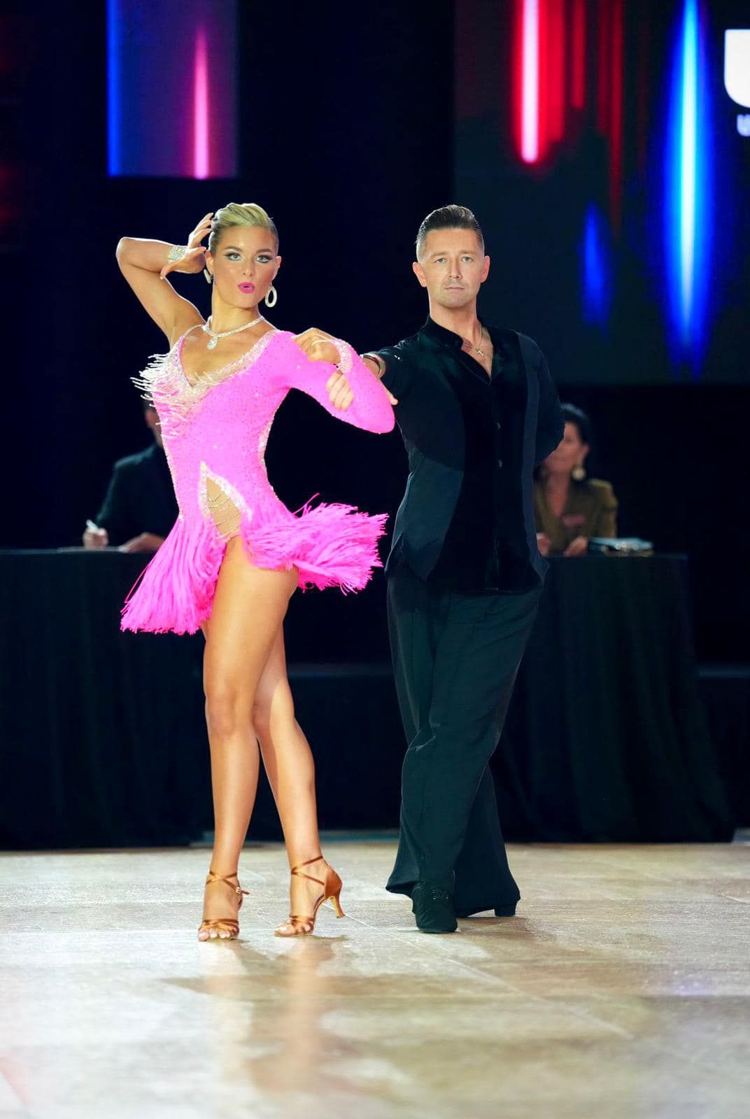 Ballroom dancers in pink and black costumes perform on a dance floor.