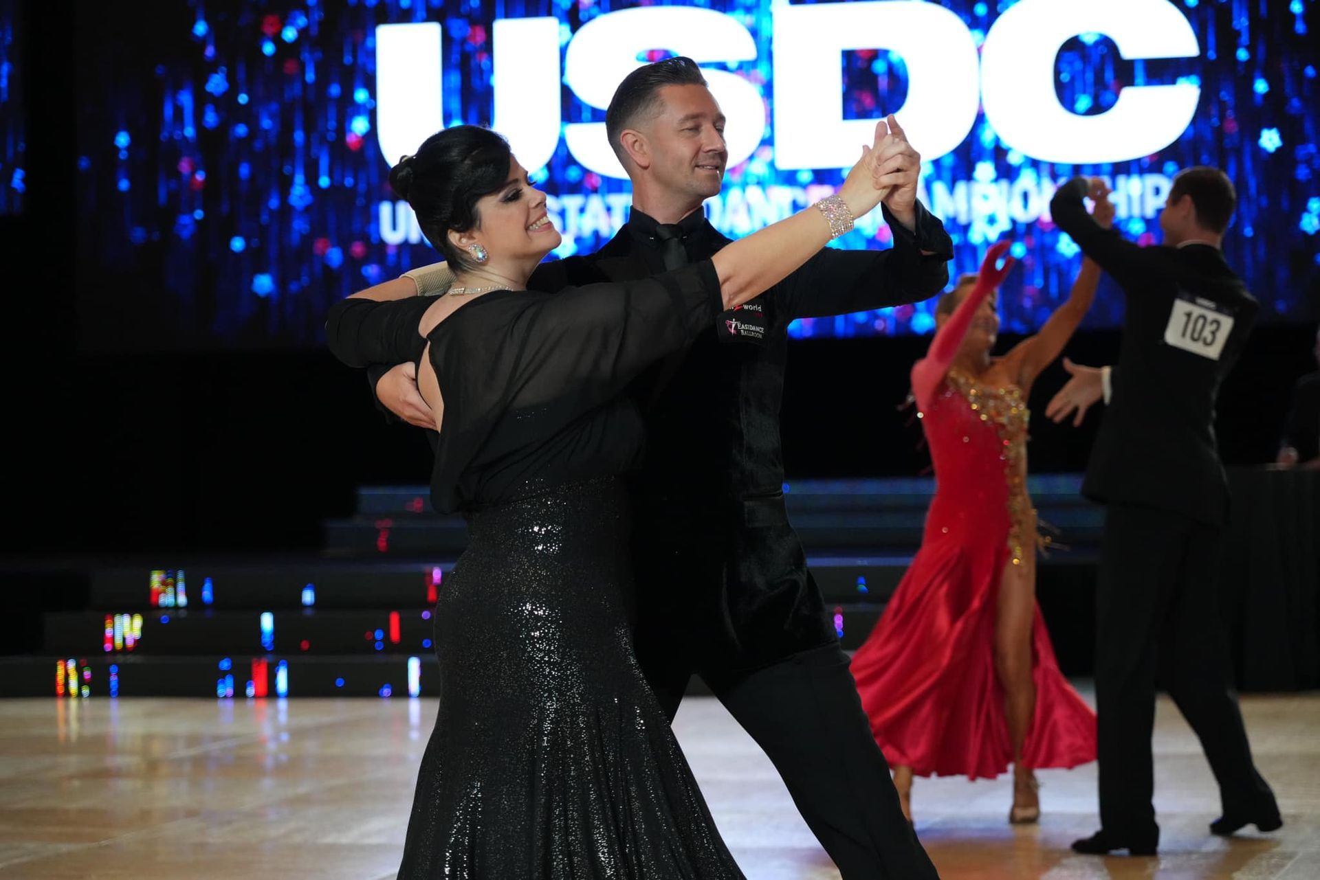 Couple in black evening attire ballroom dancing at a competition; 