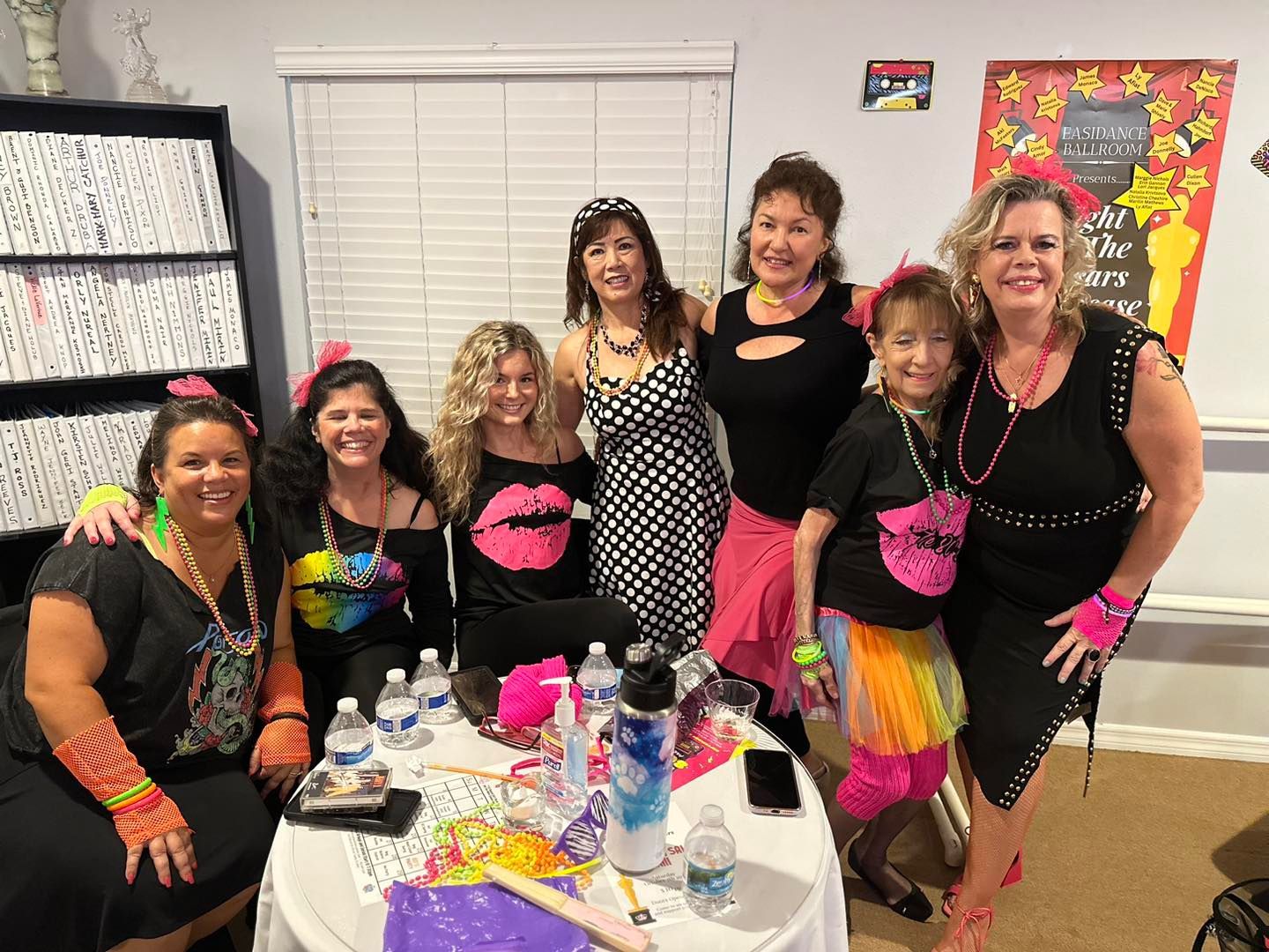 Group of women dressed in 80s attire, smiling and posing at a party with neon accessories.