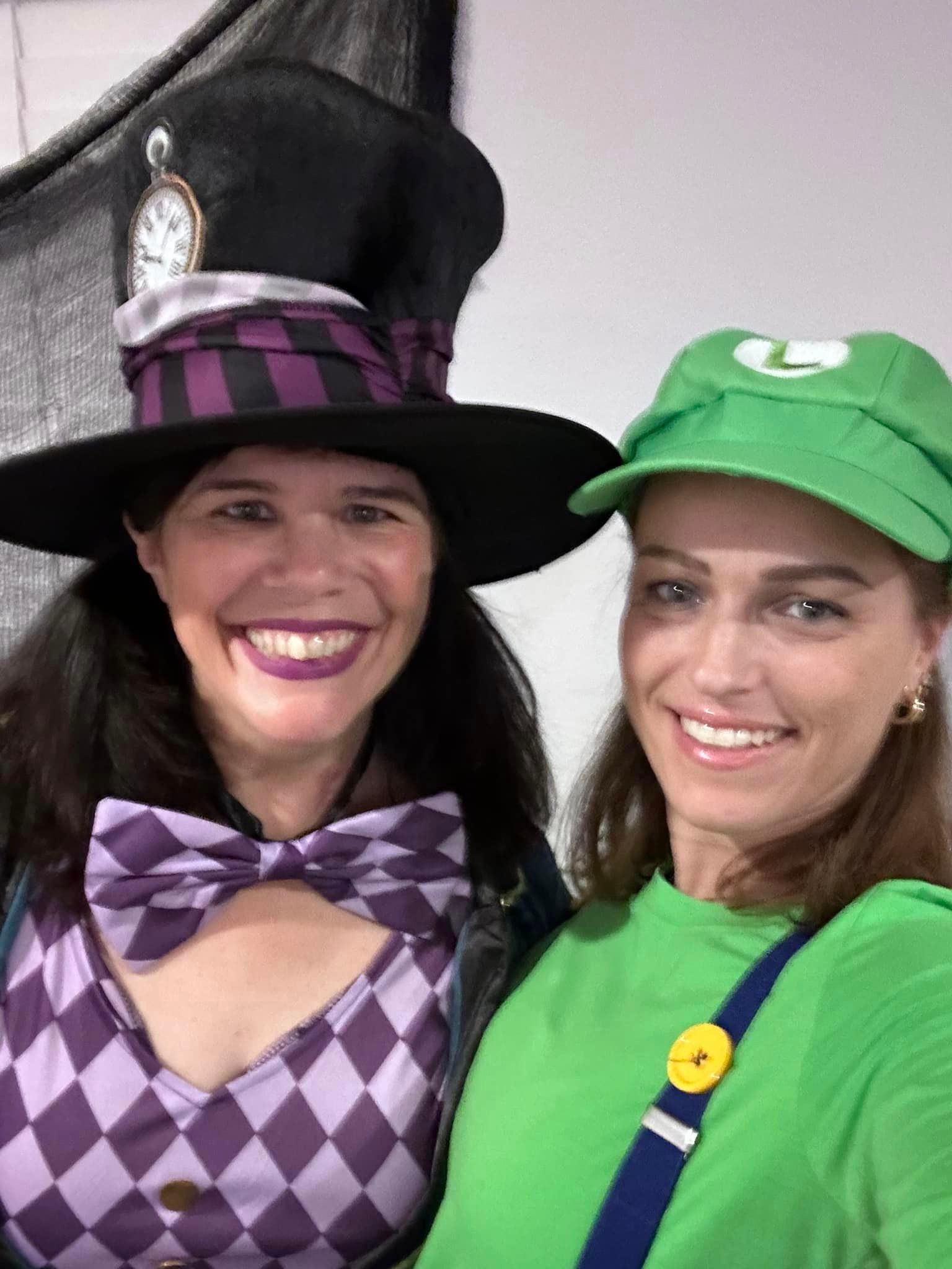 Two women in costumes: one as the Mad Hatter, one as Luigi, smiling.