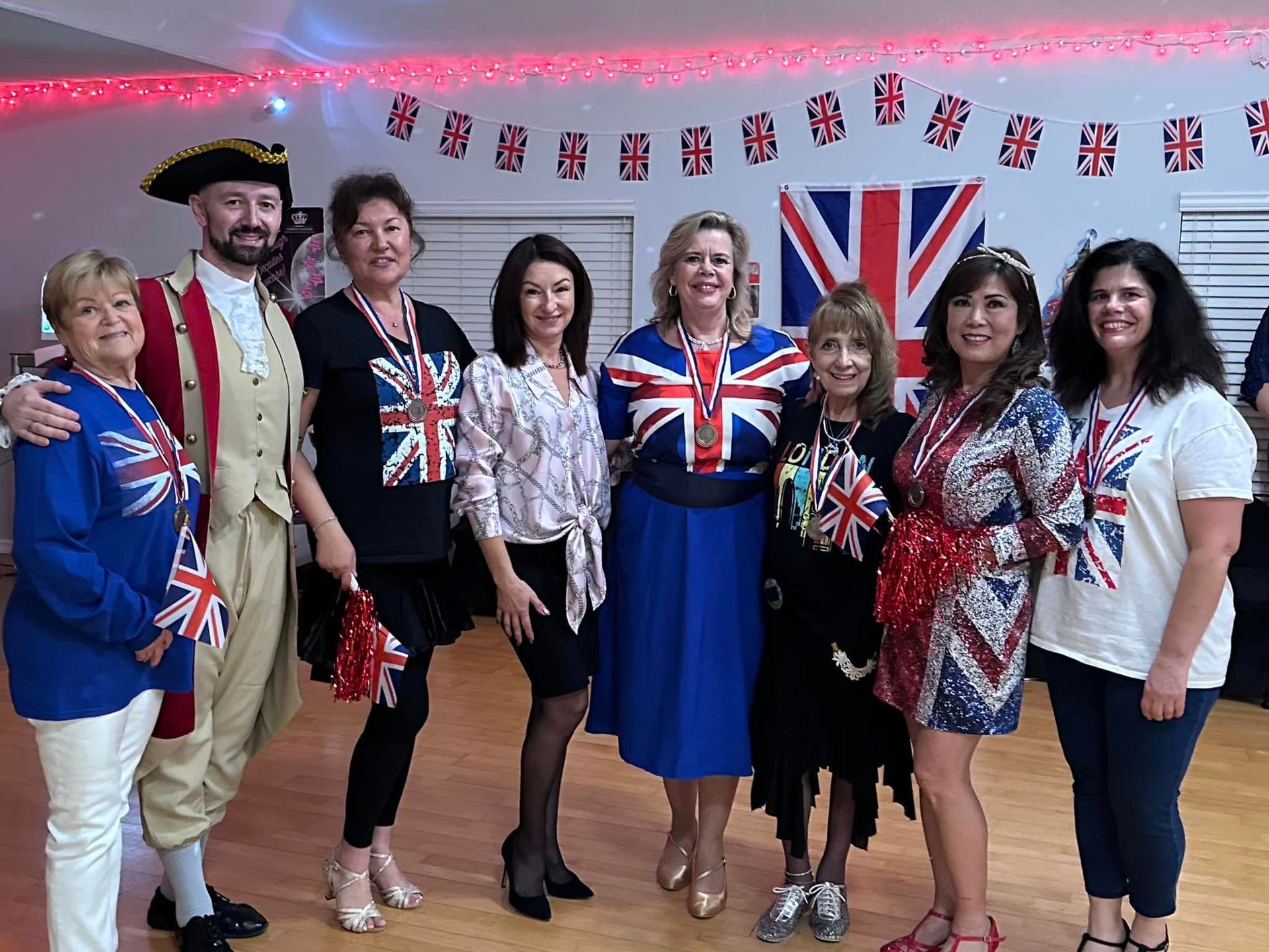 Group of people in British-themed attire posing for photo. Flags and decorations in the background.