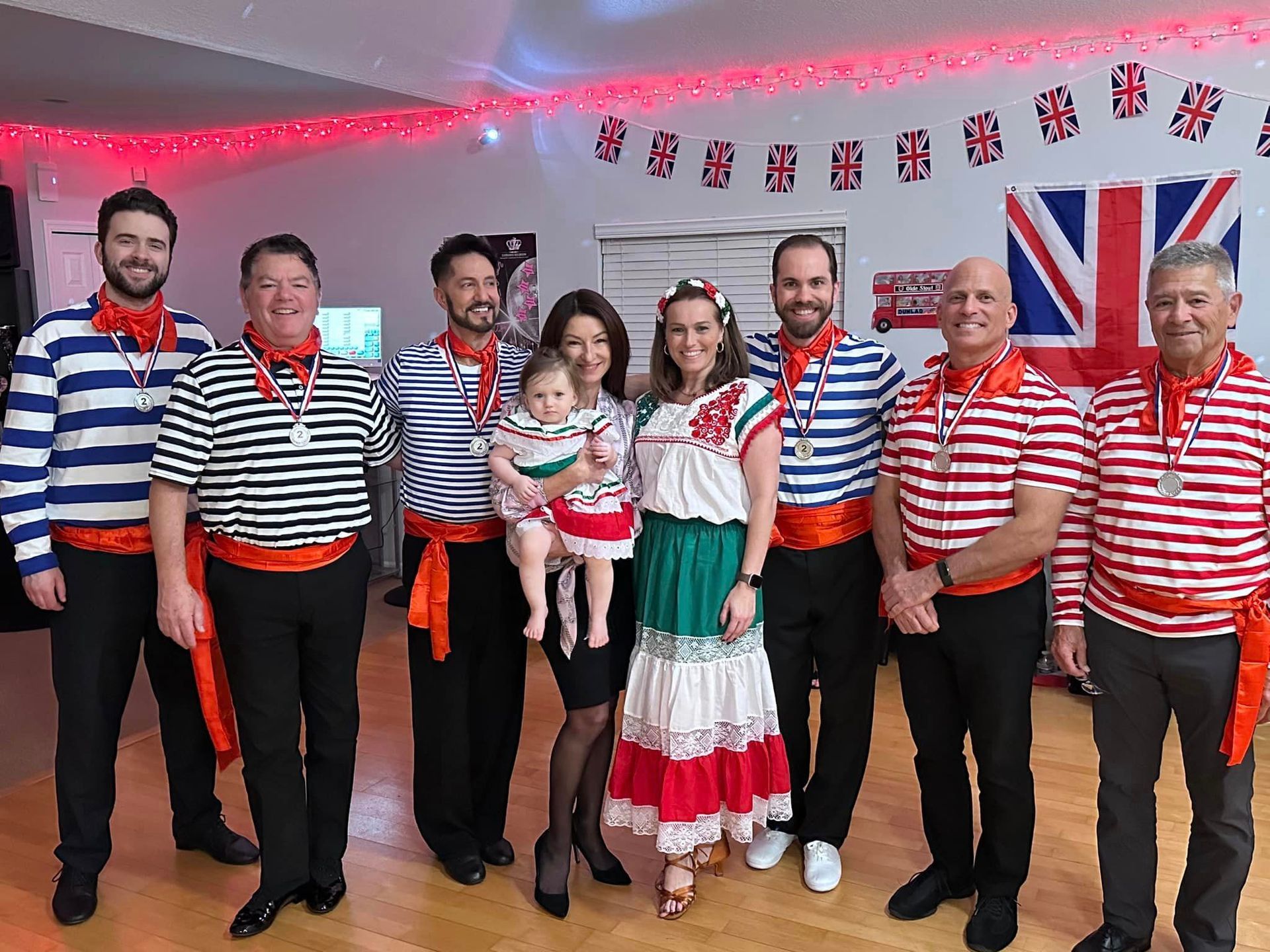 Group of people in costume with a baby posing for a photo indoors. British flag in the background.