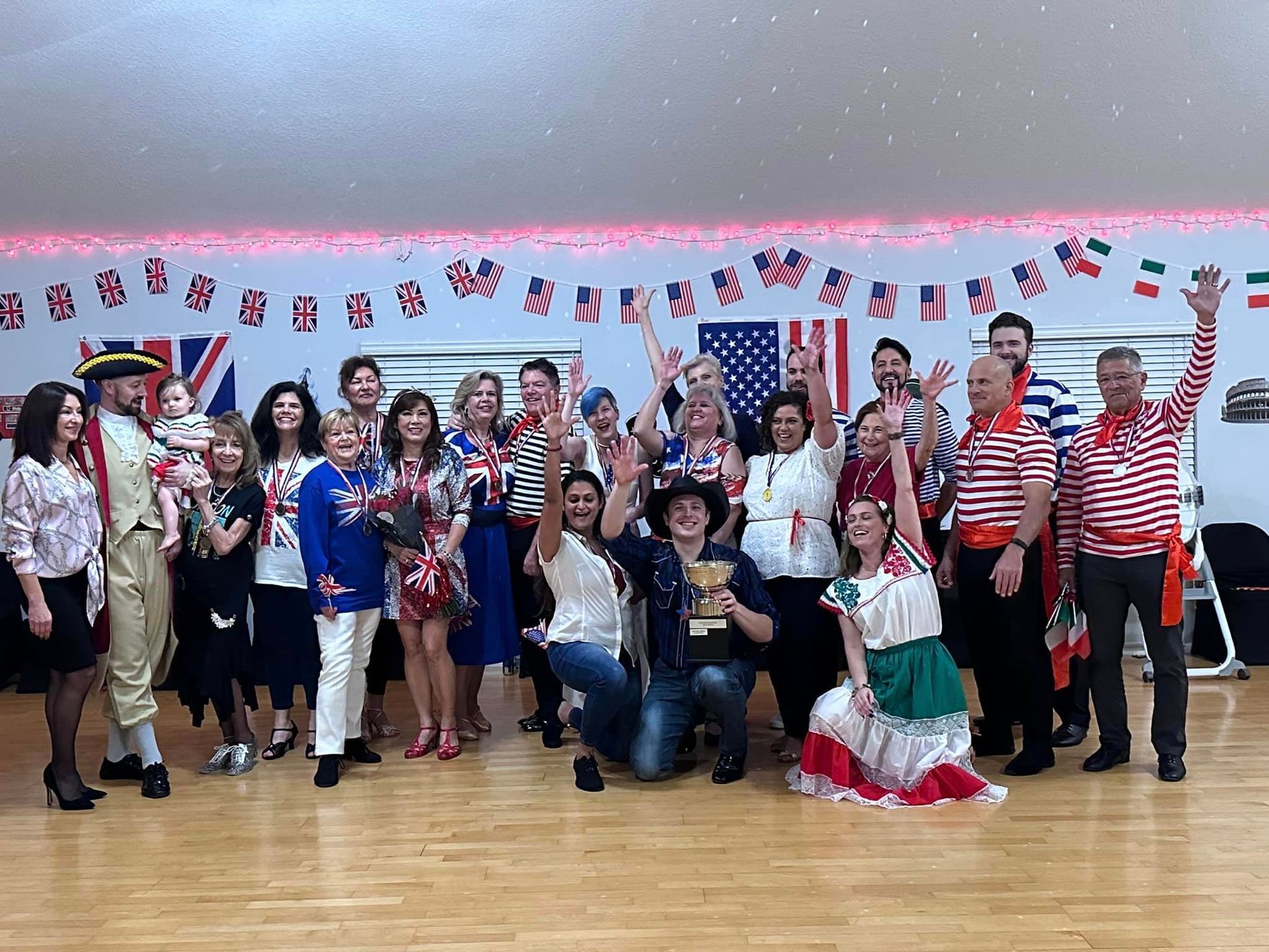 Group of people in costumes with flags, raising arms, smiling in a dance studio.