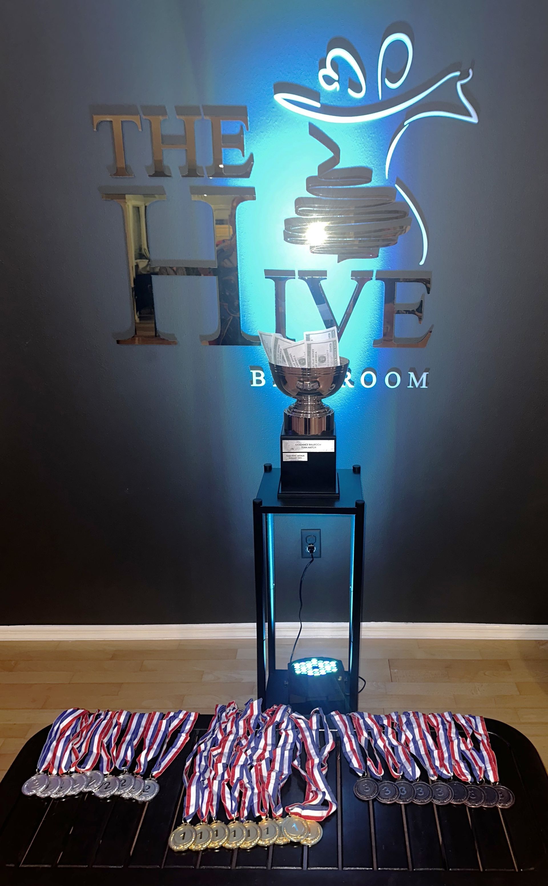 A dance trophy on a black stand with medals below, in front of 