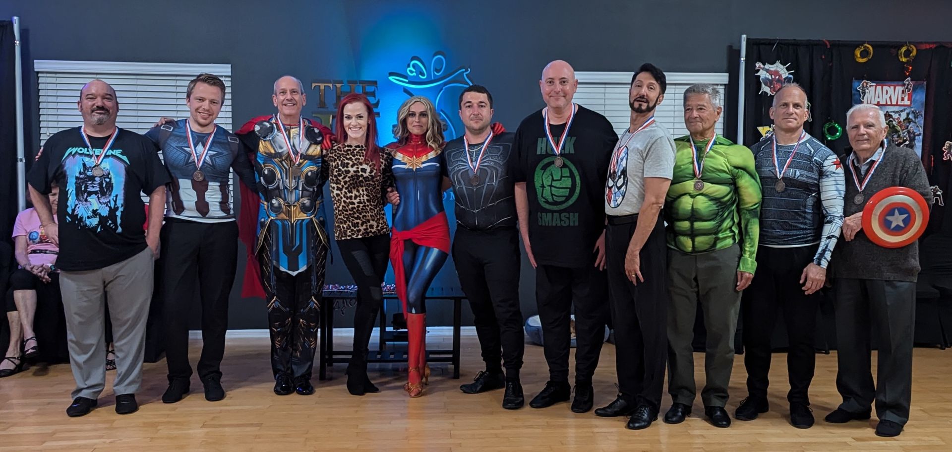 Group of people in superhero costumes posing for a photo in a room, some holding props.