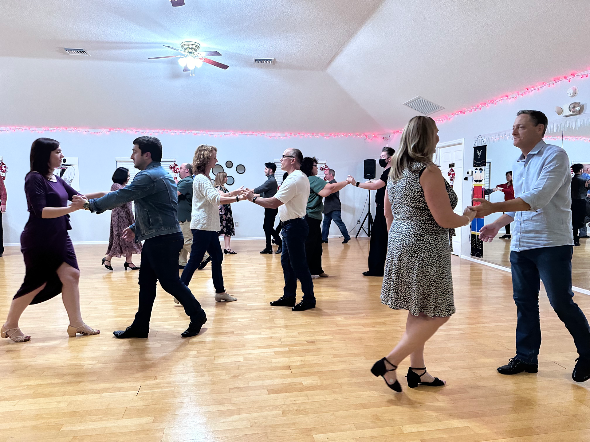 People dancing in a dance studio with a wooden floor, holding hands, and smiling.