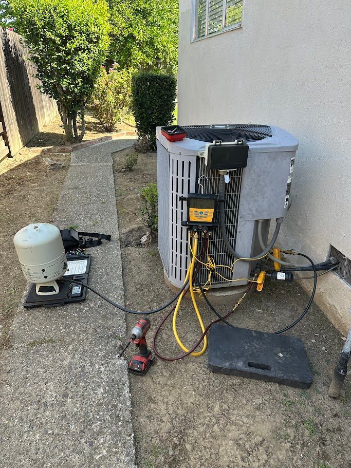 Outdoor HVAC unit with exposed wiring and tools beside a house on a gravel side yard