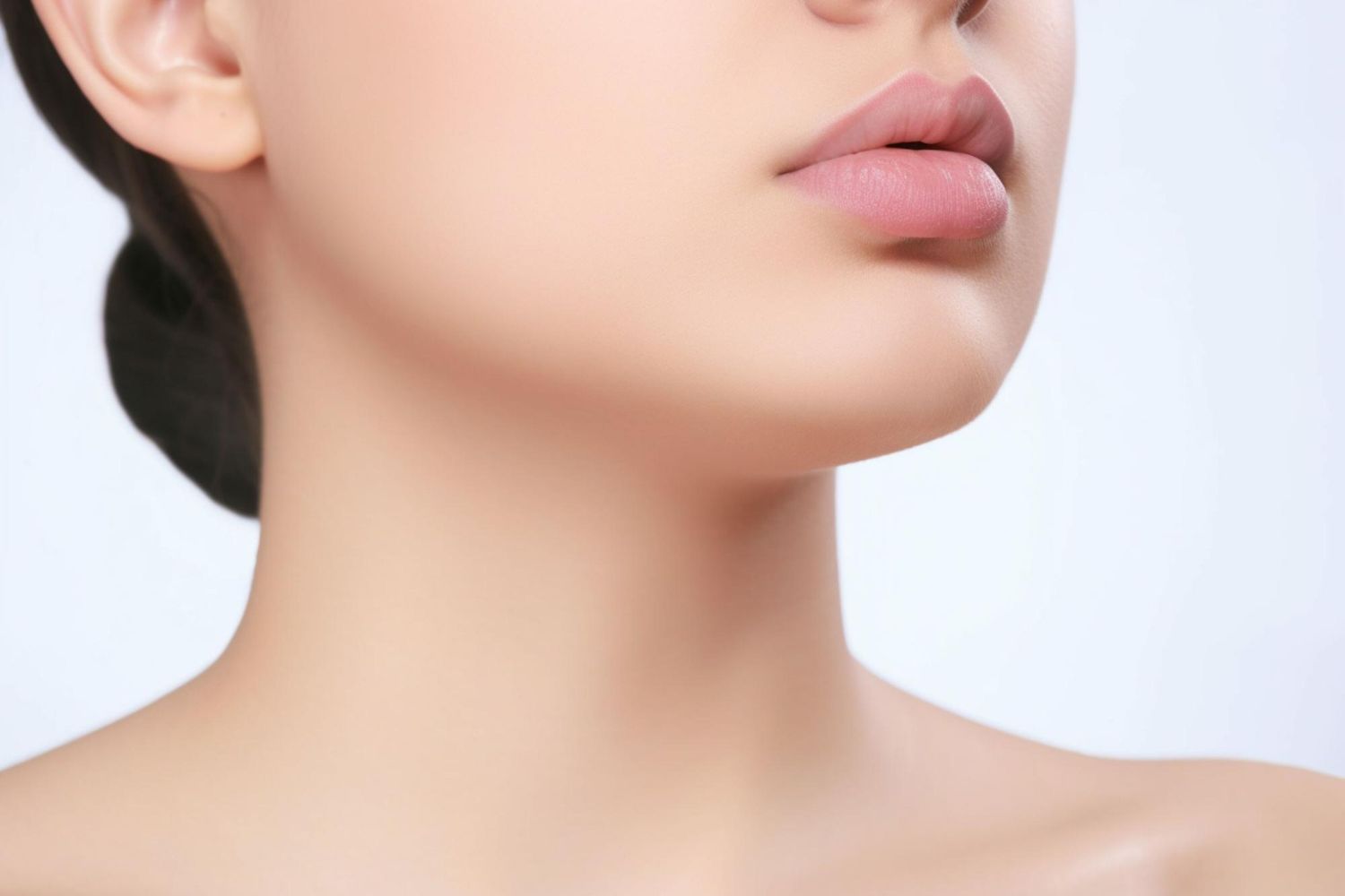 Close-up view of a person’s smooth, clear skin from the neck up, highlighting the jawline and lips against a light backdrop.