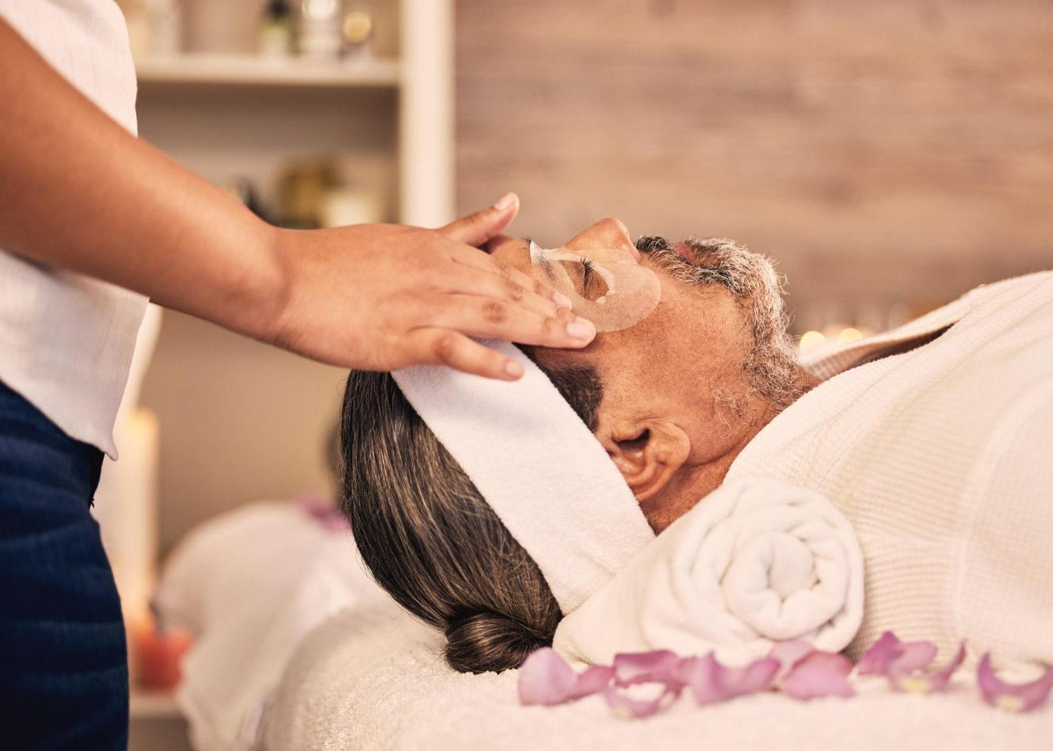 A professional massage therapist gently applies a facial treatment to a client lying down in a spa setting.