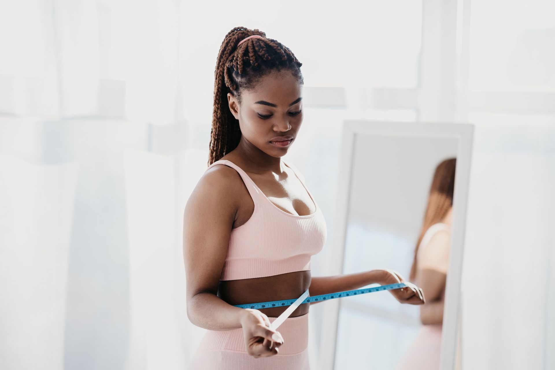 A woman is measuring her waist with a tape measure in front of a mirror.