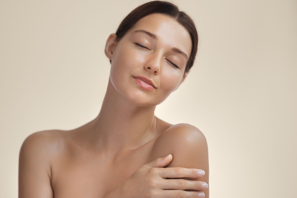 A person with smooth, clear skin, eyes closed, and a serene expression, gently touching their shoulder.