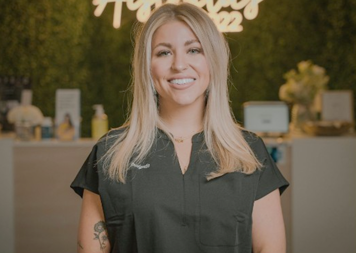 A woman in a black scrub top is smiling in front of a green wall.