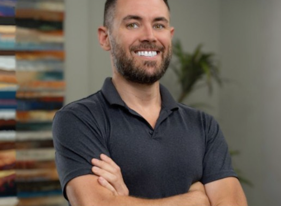 A man with a beard is standing with his arms crossed and smiling.