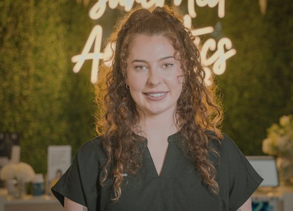 A woman with curly hair is standing in front of a green wall.