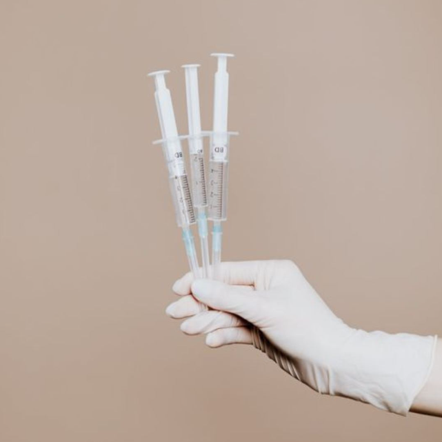 A person wearing gloves is holding three syringes in their hand.