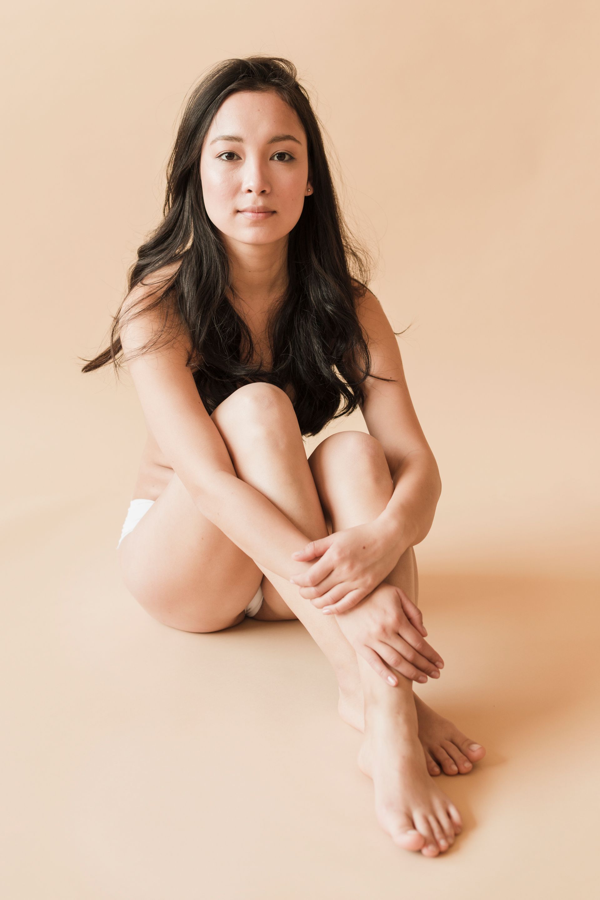 Asian woman witting on the floor holding legs