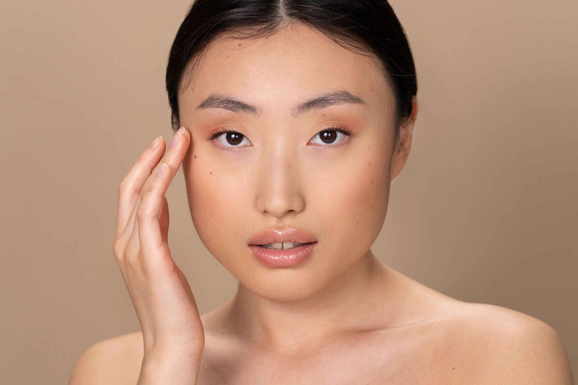 A woman is touching her face with her hand and looking at the camera.