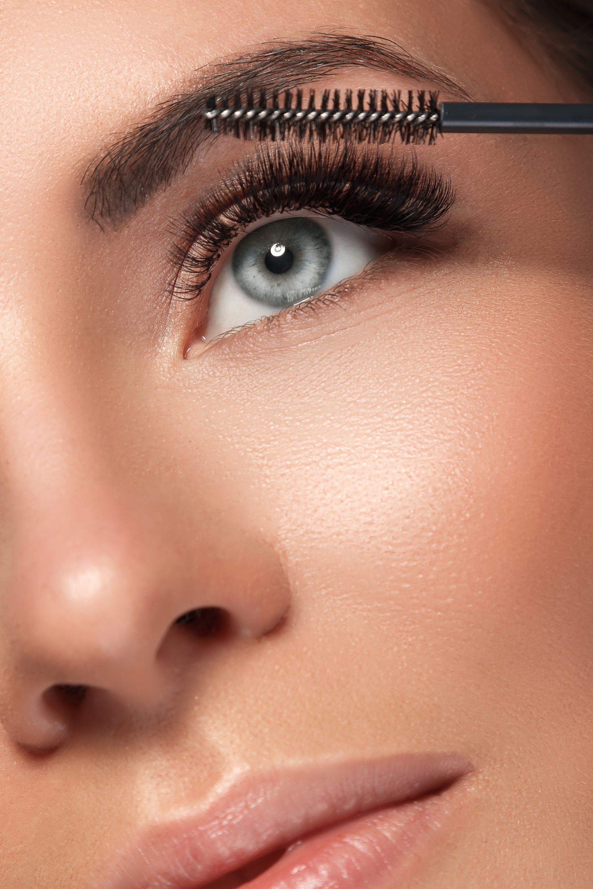 A close up of a woman applying mascara to her eyelashes.