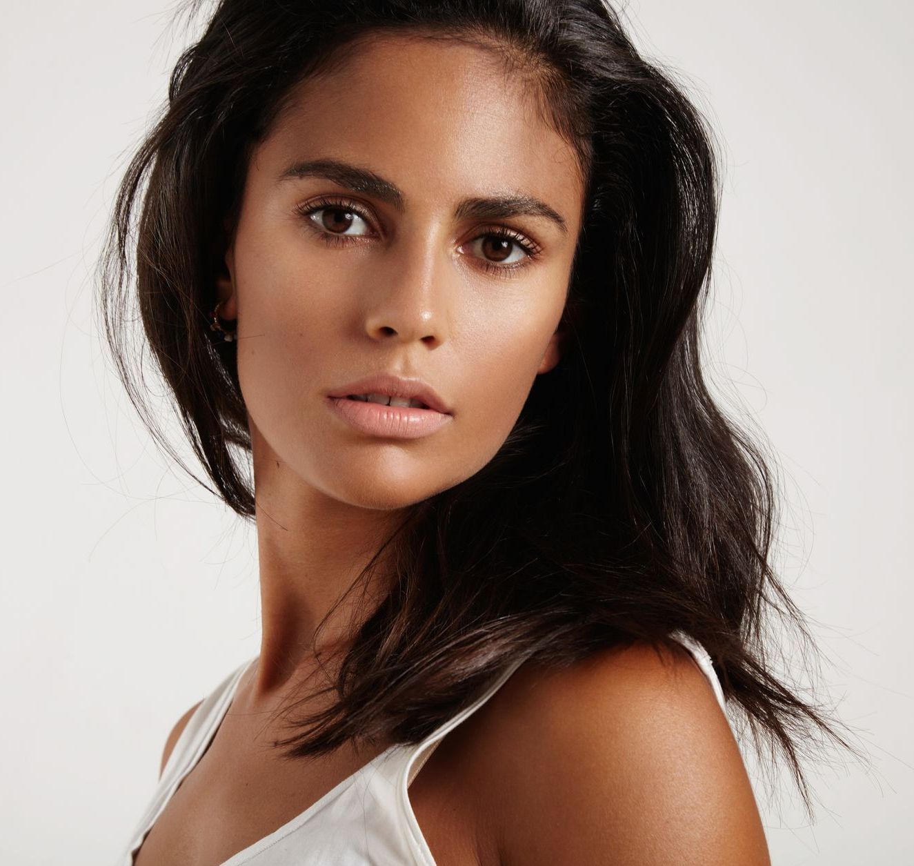 A woman with long dark hair is wearing a white tank top