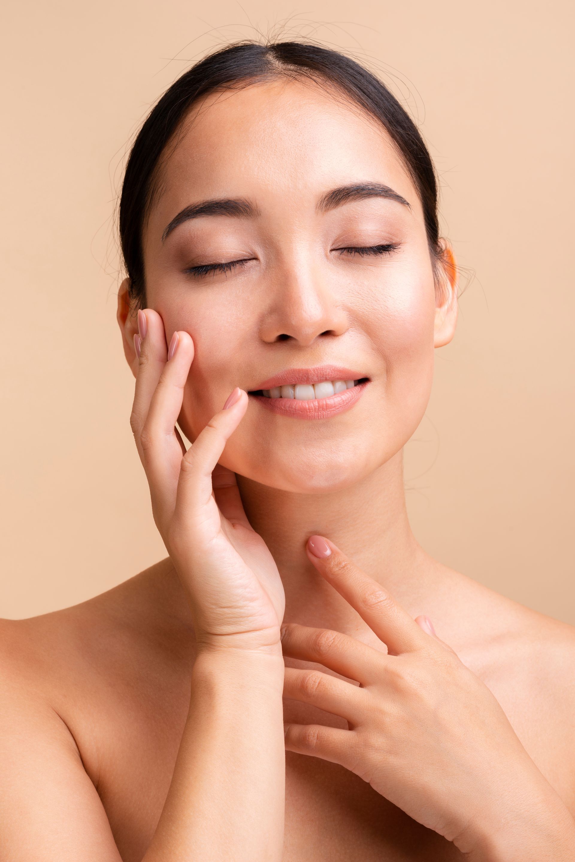 A woman is touching her face with her hands and smiling with her eyes closed.