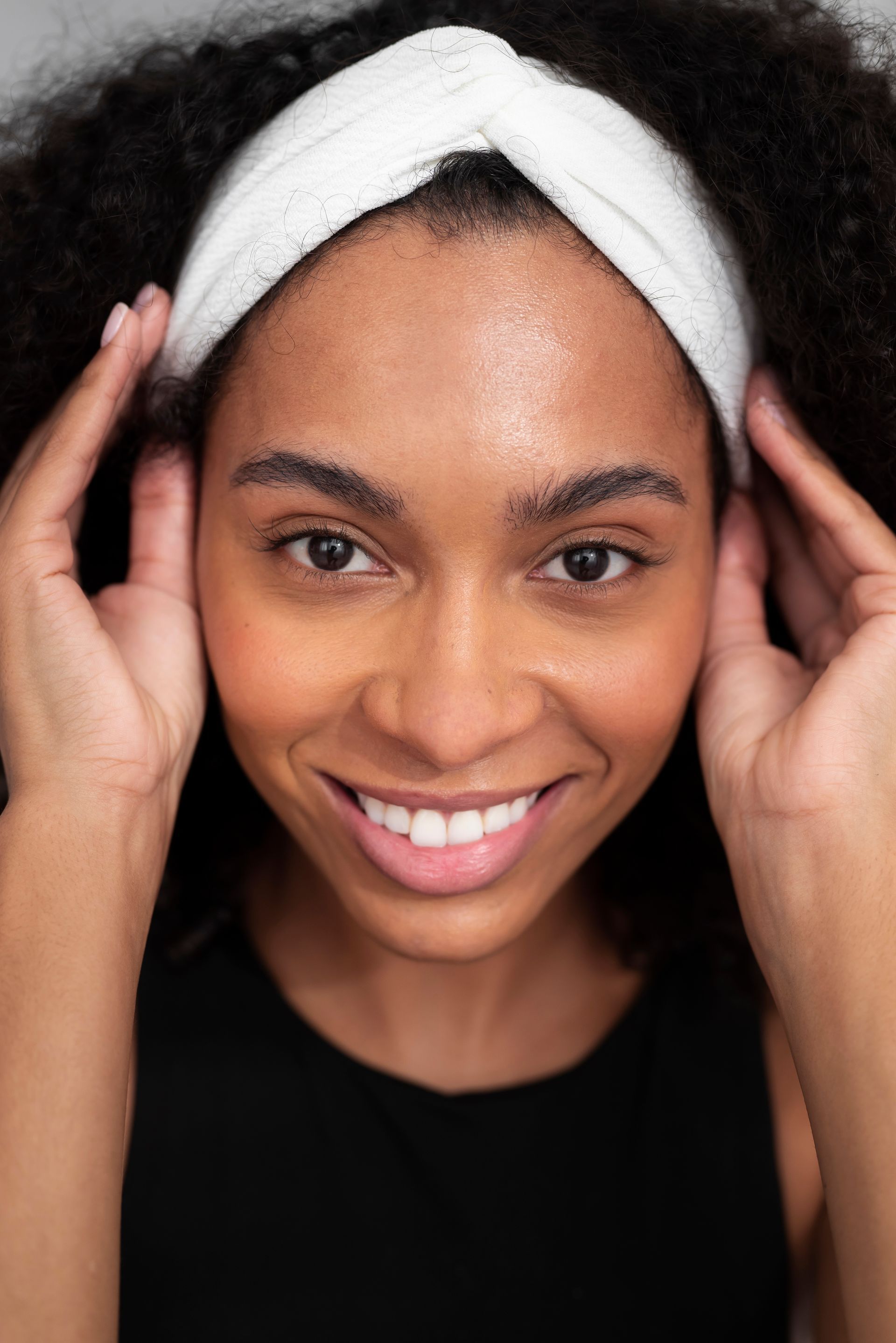 A woman is wearing a white headband and smiling.